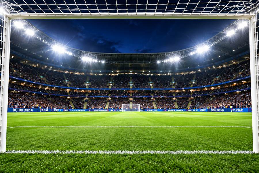 View from inside the goal towards a packed, floodlit football stadium at night